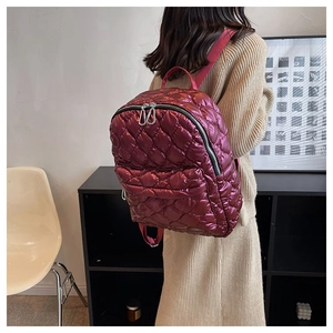 Lifestyle shot of a wine red quilted down backpack with glossy nylon finish and silver zippers