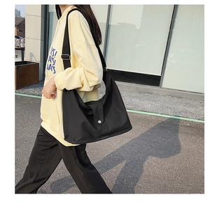 Detail of black canvas shoulder bag with adjustable metal buckle on a yellow street outfit