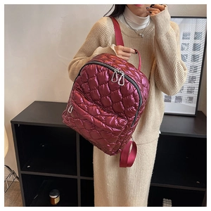 Deep red metallic quilted backpack with silver zippers shown on a beige knit dress