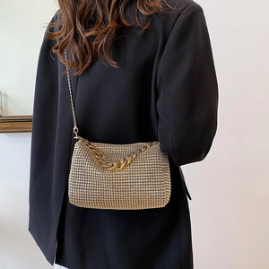 Golden rhinestone crescent crossbody bag with chain strap worn by model in black suit