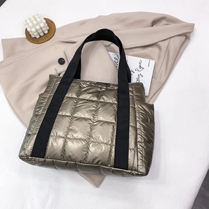 Quilted bronze tote bag with metallic finish and black strap shown on beige trench coat