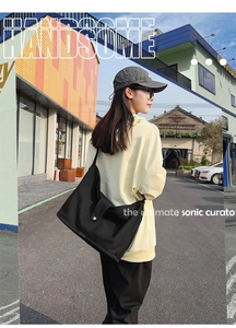 Street style view of a large black canvas tote bag with metal snap pocket detailing