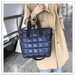 Close-up of a navy puffer tote bag with quilted square patterns and black woven handles