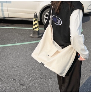Outdoor shot of a cream-colored large canvas shoulder bag with minimalist metal clasp closure
