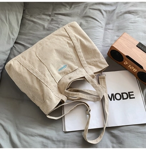 Close-up of off-white corduroy tote bag showing large front pocket and embroidered logo