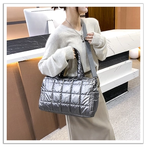 Detail view of silver quilted puffer bag with metallic finish and wide woven shoulder strap