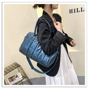 Detail view of large blue metallic quilted puffer bag with fabric shoulder strap