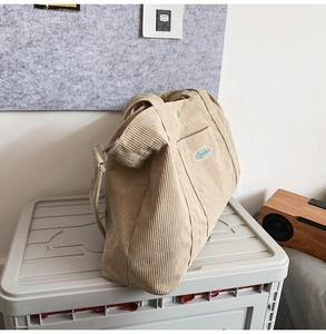 Detail of beige corduroy tote bag with side pocket and blue embroidered logo