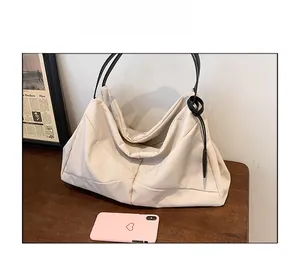Detail view of large cream canvas tote bag with black strap on wooden surface