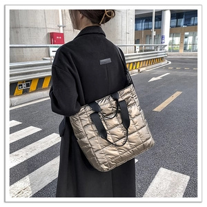 Outdoor shot of a metallic quilted tote bag with black straps worn by a person