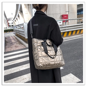 Detailed outdoor shot of a bronze quilted tote bag with black handles and shoulder strap