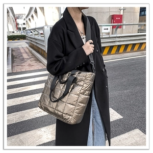 Close-up of quilted down tote bag in metallic bronze finish with black woven handles