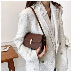 Close-up of brown leather flap crossbody bag featuring a premium gold metal clasp