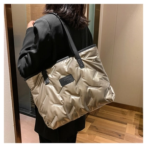Champagne gold quilted tote bag with black straps worn by a model in a warm interior