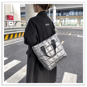 Street style shot of a large silver quilted tote bag with black woven straps for women