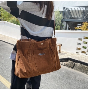 Detail of brown corduroy tote bag showing embroidered logo and texture in outdoor light