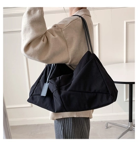 Minimalist black large capacity shoulder tote bag worn by a model in a modern interior