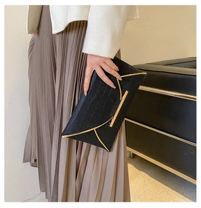 Détail de la pochette enveloppe noire à motif crocodile avec des finitions dorées