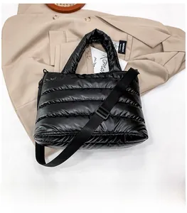 Detail shot of black quilted puffer tote bag on beige coat background with woven strap