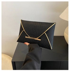 Détail d'une pochette enveloppe noire à texture crocodile avec garniture dorée chic