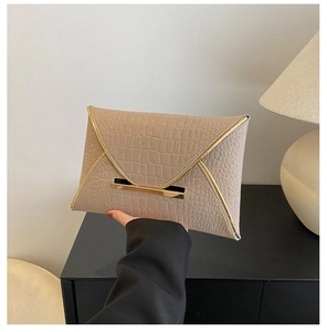 Détail d'une pochette enveloppe beige avec motif crocodile, bord dorée et fini texturé