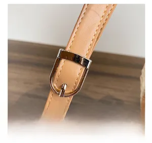 Détail d'une bandoulière en cuir camel réglable avec boucle argentée et couture jaune