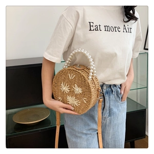 Détail du sac rond en paille avec anse en perles et broderie florale tissée