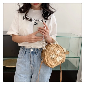 Détail d'un sac rond en paille avec broderie florale blanche et anse en chaîne de perles