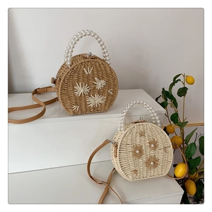 Détail de sacs ronds en paille avec poignées en perles et broderies de fleurs sur socle