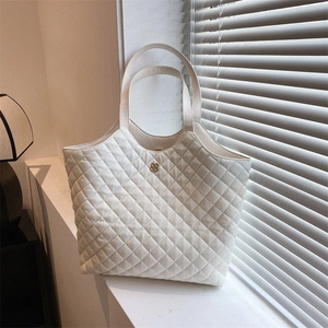 Elegant white quilted tote bag for women with gold clover buckle in a sunlit window