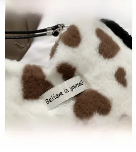 Macro shot of white plush bag detail with brown hearts and 'Believe in yourself' label