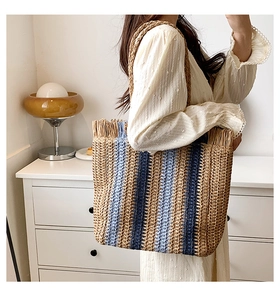 Dettaglio borsa tote in paglia intrecciata con strisce blu e bordo a frange
