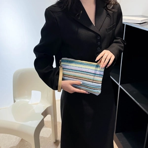 Rainbow woven clutch with wrist strap and metal zipper held by a model in a black suit
