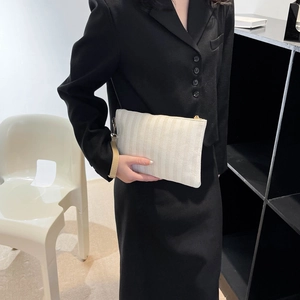 Close-up of beige striped woven clutch bag with gold zipper and wrist strap