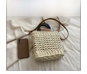 Detail view of woven straw handbag with wooden handle and a smartphone for size reference