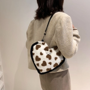 Detail view of heart-shaped plush shoulder bag with cow print and stylish text label