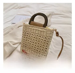 Close-up of beige straw woven handbag featuring dark wood handles and leather strap