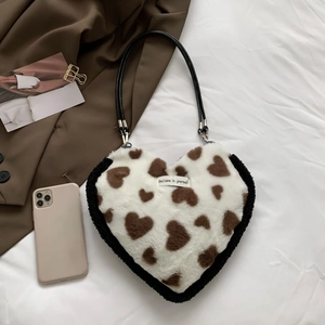 Detail of plush heart-shaped bag with slogan label on white fabric background