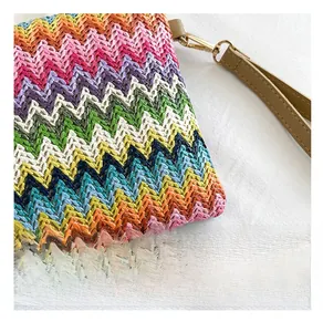 Detail of colorful woven clutch bag featuring vibrant wave patterns and faux leather wristlet