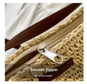 Detail of smooth metal zipper and brown leather strap on woven straw beach bag