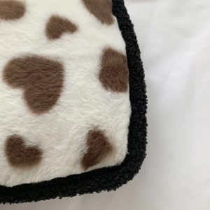 Close-up of white plush fabric with brown heart spots and black sherpa trim detail
