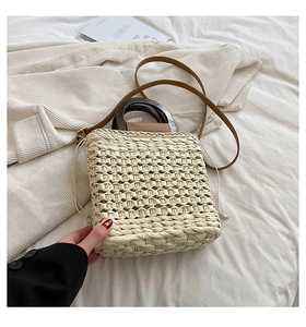 Detail of hand-woven beige straw bag with round wooden handles and adjustable shoulder strap