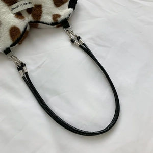 Detail of cow print faux fur bag with black leather handle and silver metal clasp