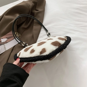 Detail of plush heart-shaped bag featuring cow print texture and black leather strap
