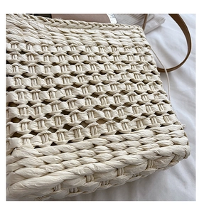 Close-up of beige woven straw handbag showing detailed natural texture and brown leather strap