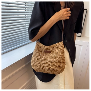 Détail du sac en paille tissée avec écusson en cuir brun sur une tenue noir et blanc