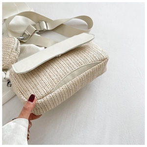 Detail of beige straw woven crossbody bag with white PU trim and mini coin purse charm