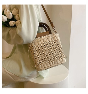 Detail of woven straw handbag featuring round wooden handles and adjustable leather strap