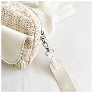 Close-up of woven straw crossbody bag with white leather flap and metal zipper details
