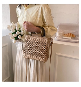 Detail of a woven straw tote bag with brown wood handle and crossbody strap in a French setting